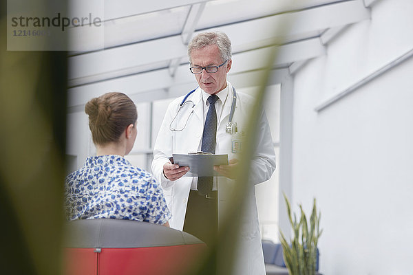Männlicher Arzt mit Klemmbrett im Gespräch mit Patientin in der Lobby des Krankenhauses