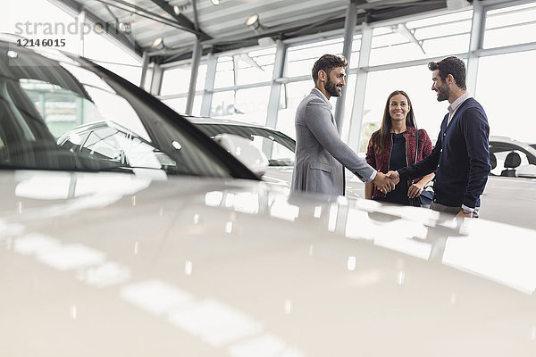 Autoverkäufer beim Händeschütteln mit ein paar Kunden im Autohaus-Showroom