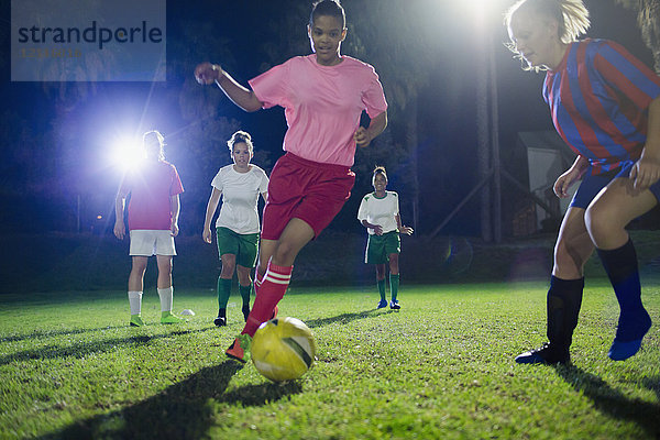 Junge Fußballspielerinnen  die nachts auf dem Spielfeld spielen und den Ball treten.