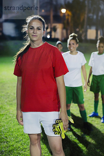 Portrait selbstbewusste junge Fußballspielerin auf dem Spielfeld bei Nacht