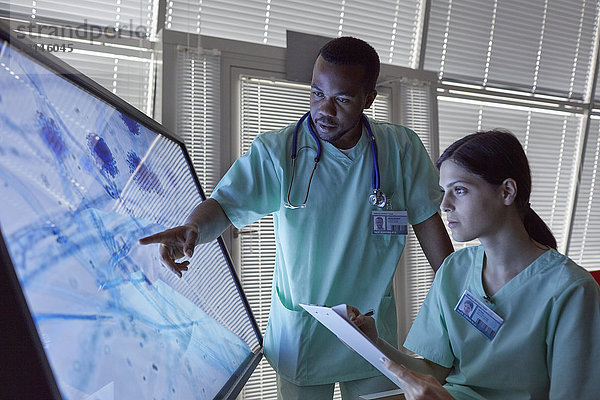 Krankenschwestern mit Zwischenablage zur Untersuchung eines vergrößerten Objektträgers am Computerbildschirm