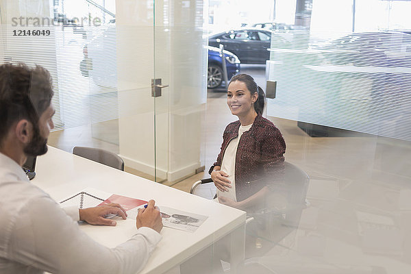 Autoverkäufer im Gespräch mit schwangeren Kunden im Autohausbüro