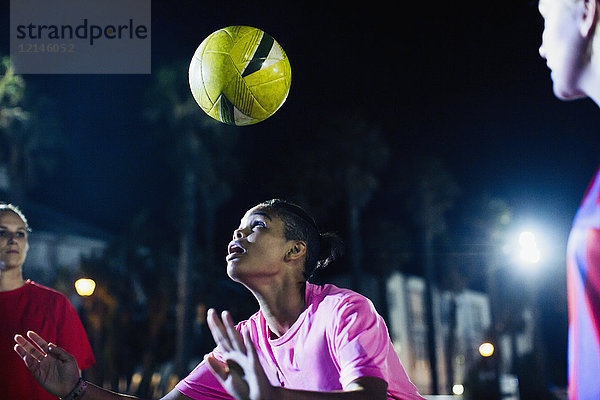Junge Fußballspielerin  die nachts den Ball auf dem Spielfeld anführt.