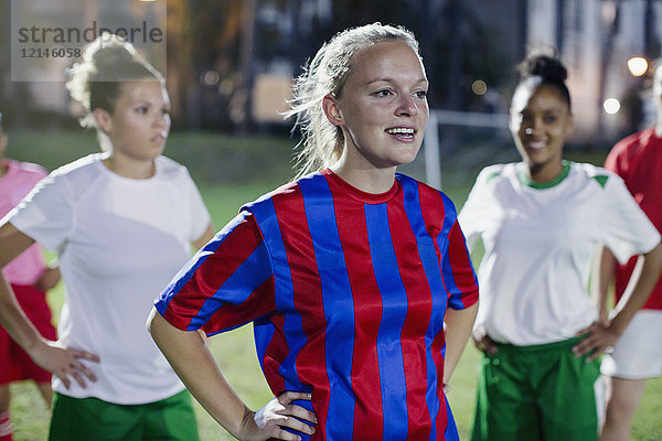 Selbstbewusste junge Fußballspielerinnen ruhen nachts mit den Händen auf dem Spielfeld.