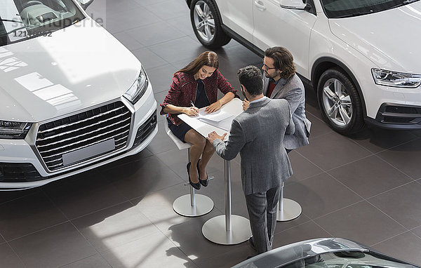 Autoverkäufer beobachtet Paar Kunden bei der Unterzeichnung finanzieller Vertragsunterlagen im Autohaus-Showroom