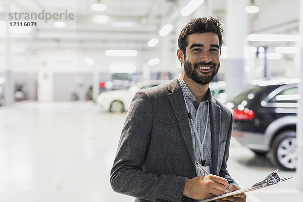 Portrait lächelnder  selbstbewusster Autoverkäufer mit Klemmbrett in der Autowerkstatt