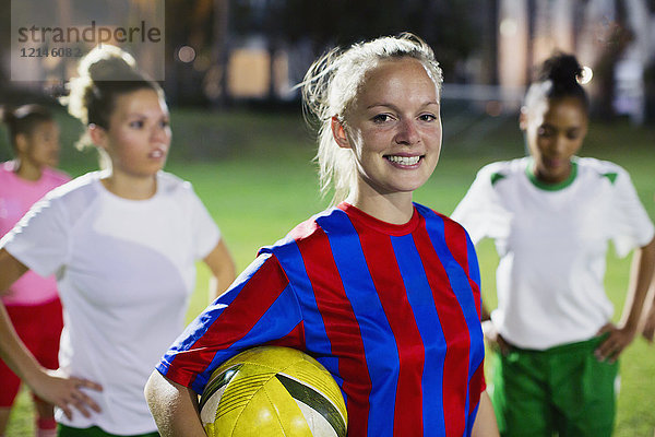 Portrait lächelnde  selbstbewusste junge Fußballspielerin mit Ball auf dem Spielfeld bei Nacht