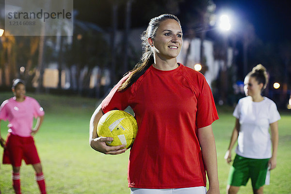 Portrait selbstbewusste  lächelnde junge Fußballspielerin auf dem Spielfeld bei Nacht