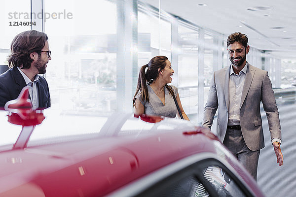 Autoverkäufer und lächelndes Paar Kunden  die sich ein neues Auto im Autohaus anschauen.