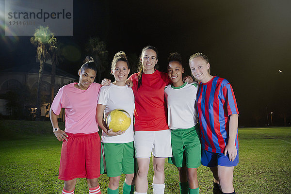 Portrait lächelnde  selbstbewusste junge Fußballerinnen mit Ball auf dem Spielfeld bei Nacht