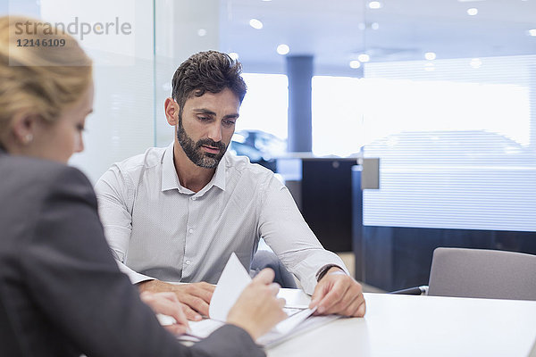 Autoverkäuferin erklärt dem männlichen Kunden im Autohausbüro die finanziellen Vertragsformalitäten