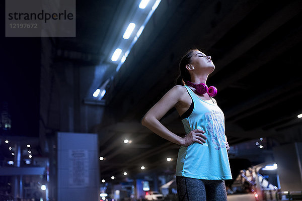 Junge Frau mit rosa Kopfhörern in moderner urbaner Umgebung bei Nacht