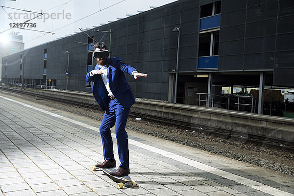 Junger Mann mit Longboarding am Bahnhof  mit VR-Brille