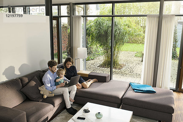Eltern und Sohn sitzen auf dem Sofa im modernen Wohnzimmer mit Laptop zu Hause