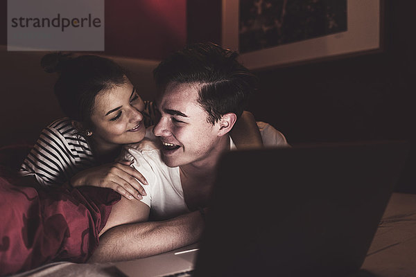 Glückliches Paar im Bett liegend zu Hause mit Laptop