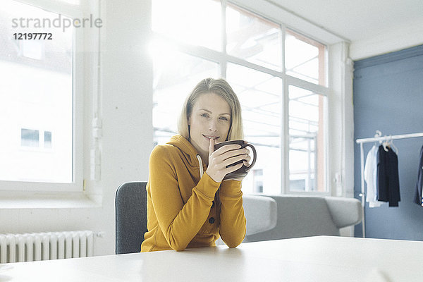 Porträt der Modedesignerin am Schreibtisch in ihrem Atelier bei einer Tasse Kaffee