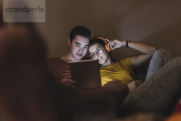 Paar mit Kopfhörer und Tablett zum Entspannen auf der Couch zu Hause