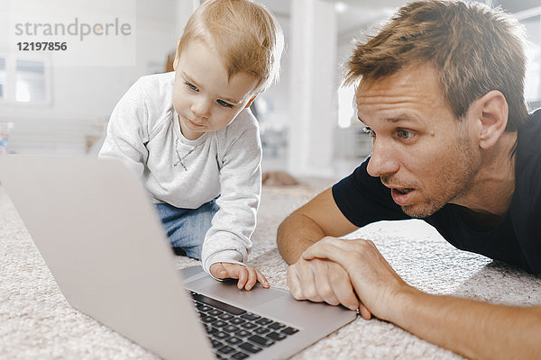 Erstaunlicher Vater mit kleiner Tochter  die den Laptop auf dem Boden benutzt.