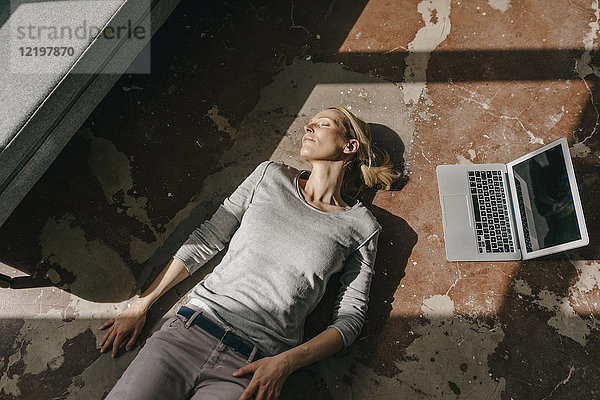 Frau schläft auf dem Boden neben dem Laptop