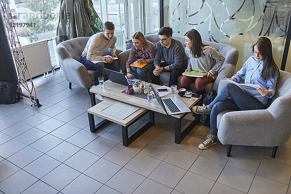 Gruppe von Freunden sitzen zusammen in einem Café mit Laptop und Dokumenten