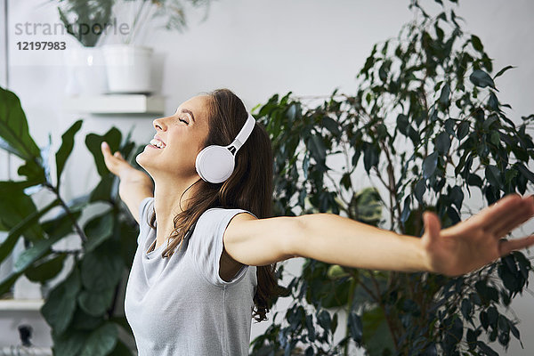 Fröhliche junge Frau mit gestreckten Armen beim Musikhören in der Zimmerpflanze