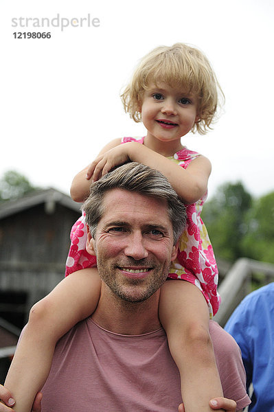 Porträt eines glücklichen Mannes  der seine kleine Tochter auf den Schultern trägt.