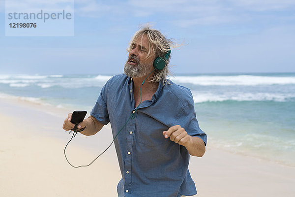 Schöner älterer Mann mit Kopfhörern  der am Strand tanzt.