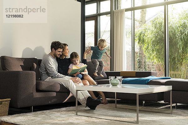 Familie auf dem Sofa zu Hause lesen Buch mit Jungen springen