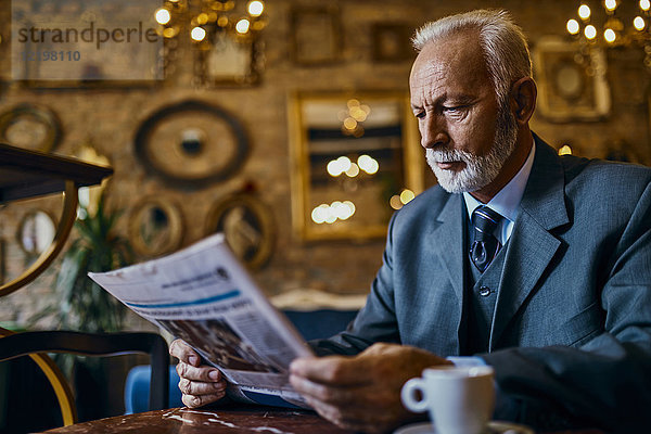 Eleganter älterer Mann beim Zeitungslesen im Café