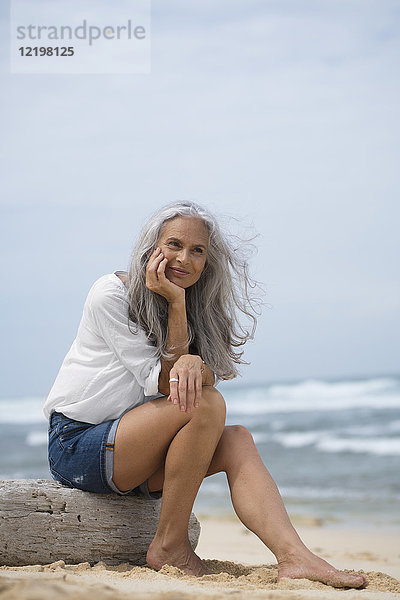 Schöne Seniorin am Strand sitzend