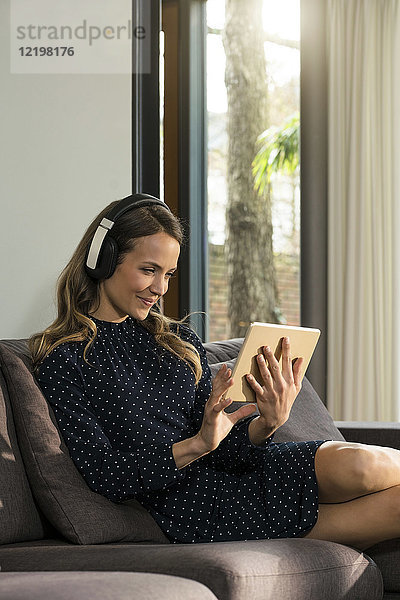 Lächelnde Frau mit Tablette und Kopfhörer zum Entspannen auf der Couch zu Hause