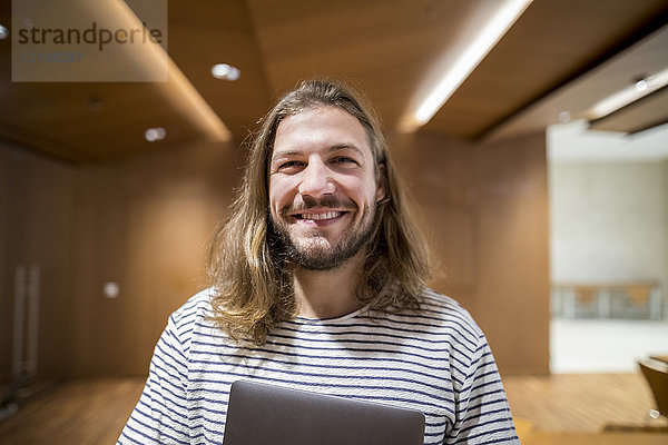 Porträt des lachenden Mannes mit Laptop in der Universität