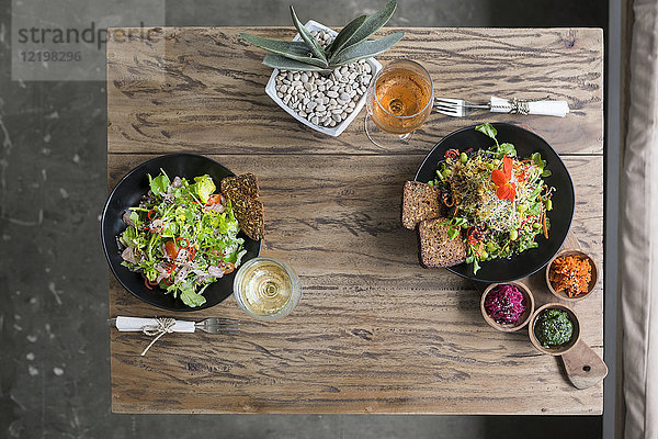 Dekorierte Salatschüsseln auf Holztisch mit Weingläsern