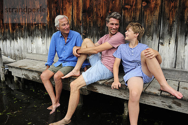 Junge sitzend mit Großvater und Vater zusammen am Steg im Sommer