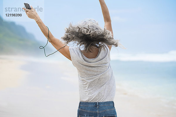 Seniorin mit Kopfhörer tanzt am Strand