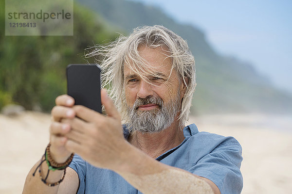 Schöner älterer Mann  der ein Foto mit dem Smartphone am Strand macht.
