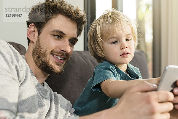 Vater und Sohn betrachten Smartphone auf der Couch zu Hause