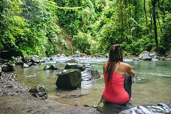 Costa Rica  Vulkan Arenal Nationalpark  Frau sitzt auf einem Stein des Flusses Fortuna
