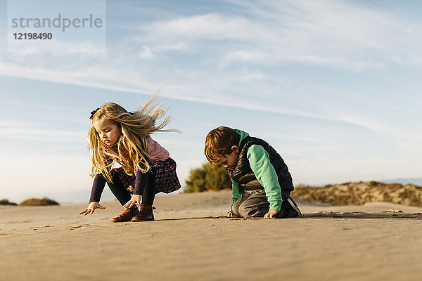 Zwei Kinder spielen im Winter mit dem Sand am Strand.
