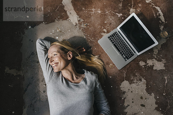 Lächelnde Frau auf dem Boden neben dem Laptop liegend