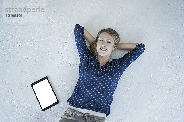 Porträt einer lächelnden jungen Frau auf dem Boden liegend mit Tablette