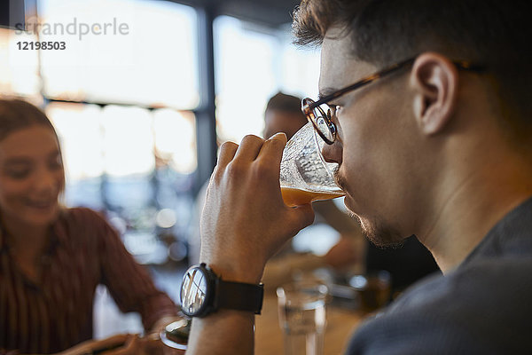 Junger Mann trinkt ein Glas Saft in einem Café mit Freunden im Hintergrund