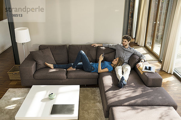 Paar mit Tablett und Smartphone zum Entspannen auf dem Sofa im modernen Wohnzimmer zu Hause