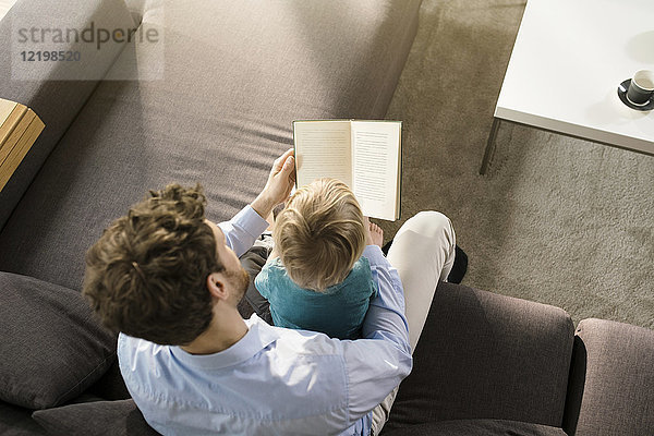 Vater und Sohn lesen Buch auf der Couch zu Hause