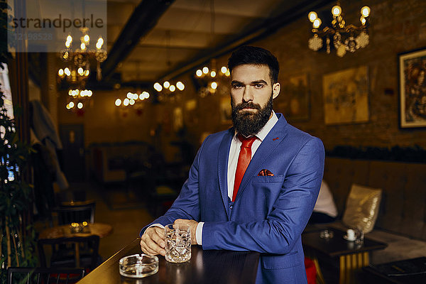 Portrait eines eleganten jungen Mannes in einer Bar mit Tumbler