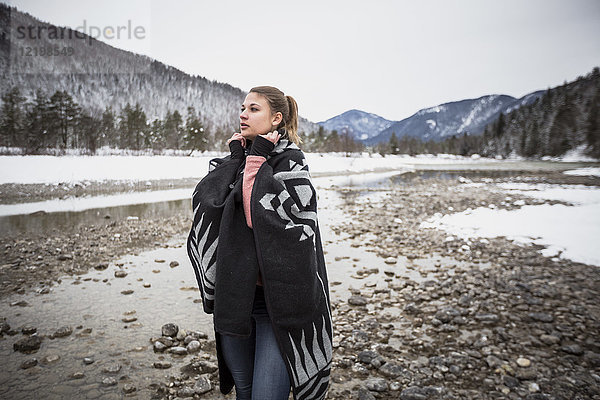 Junge Frau steht im Winter an einem Fluss