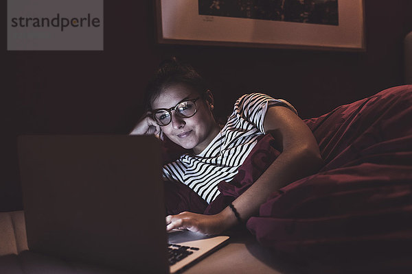 Frau im Bett liegend zu Hause mit Laptop