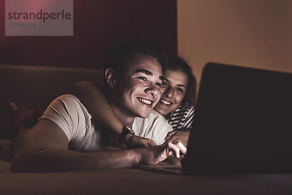 Glückliches Paar  das zu Hause im Bett liegt und auf den Laptop schaut.