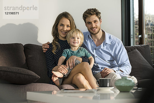 Porträt der lächelnden Eltern und des Sohnes  der zu Hause auf dem Sofa sitzt