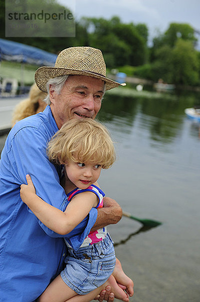 Kleines Mädchen auf den Armen ihres Großvaters am Seeufer